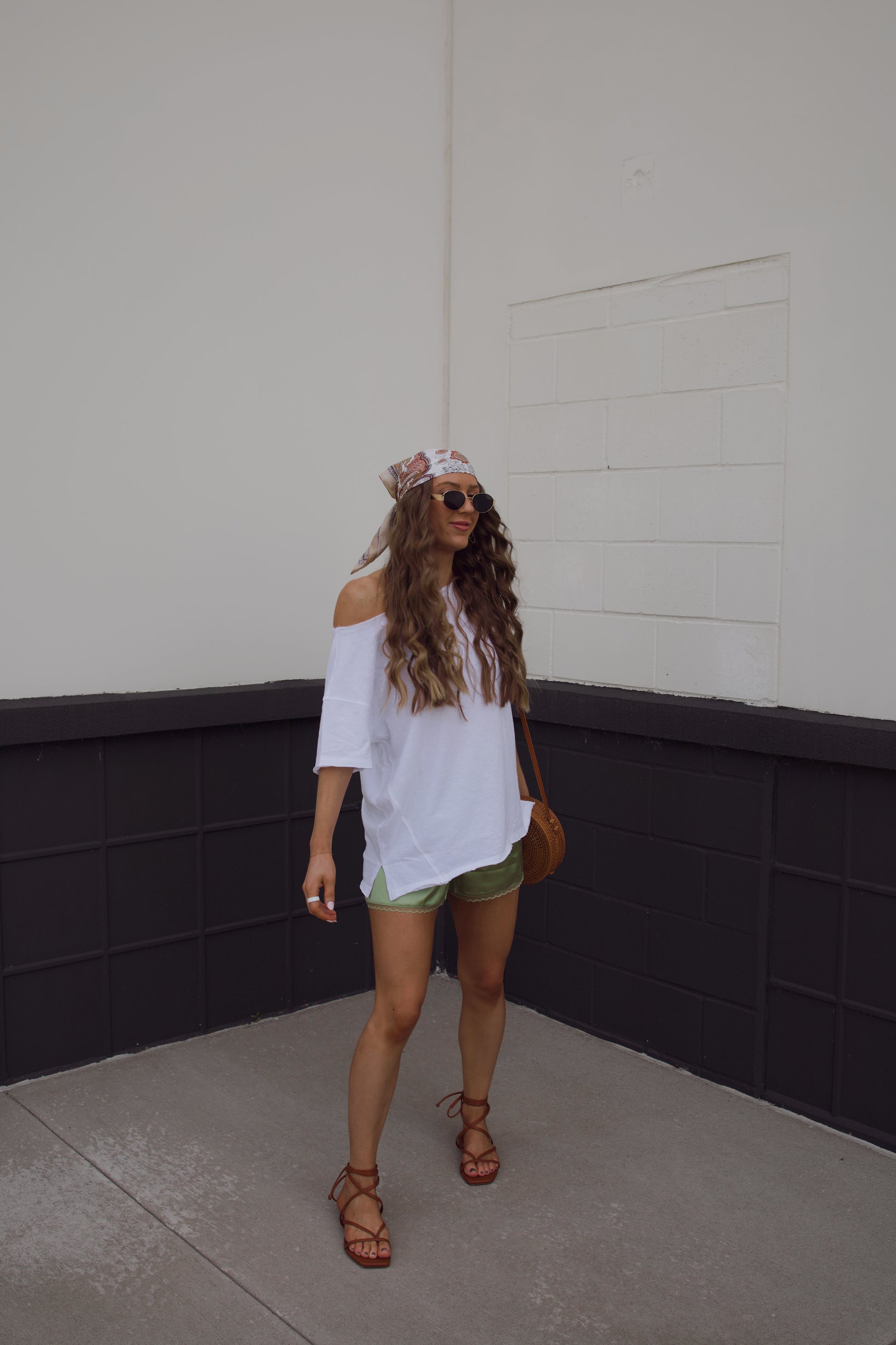 Woman in a white top and green shorts standing against a plain wall.